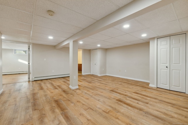 basement featuring a drop ceiling, a baseboard radiator, and light hardwood / wood-style floors