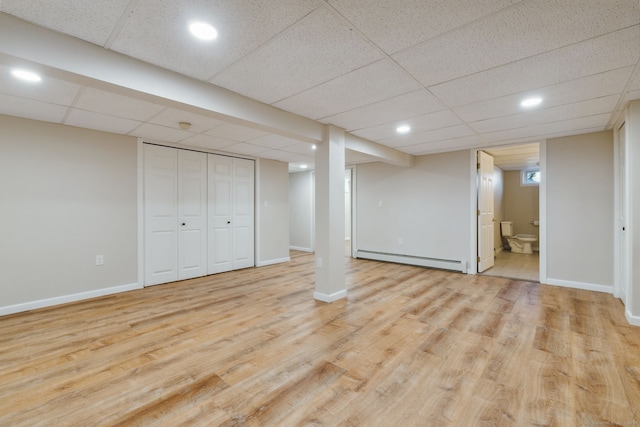 basement featuring a baseboard heating unit, a paneled ceiling, and light hardwood / wood-style floors