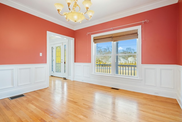 empty room featuring an inviting chandelier, crown molding, and light hardwood / wood-style floors