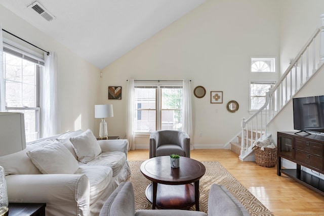 living area with light wood finished floors, visible vents, stairway, high vaulted ceiling, and baseboards