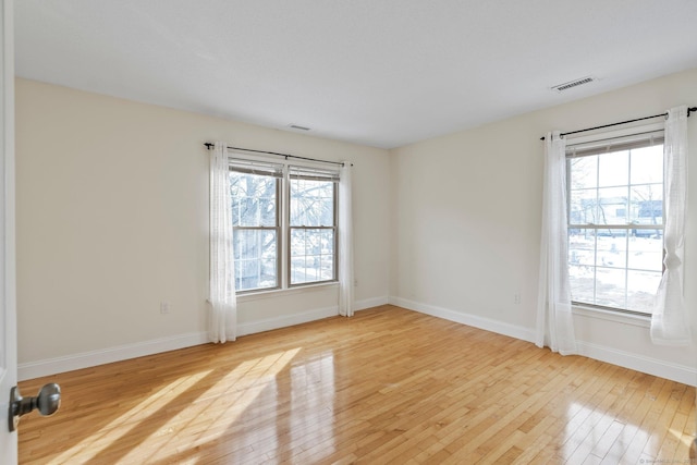 empty room featuring a healthy amount of sunlight, visible vents, and light wood-style flooring