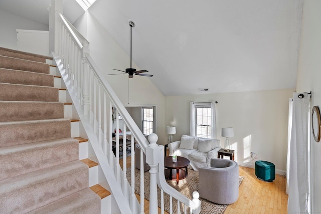 living area featuring ceiling fan, high vaulted ceiling, wood finished floors, visible vents, and stairs