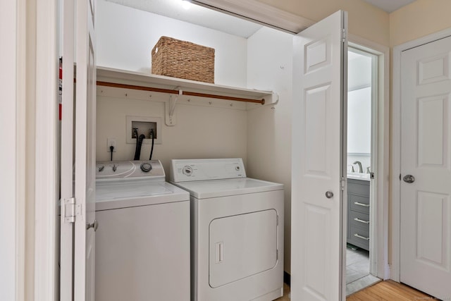 laundry area featuring laundry area, washing machine and dryer, light wood finished floors, and a sink