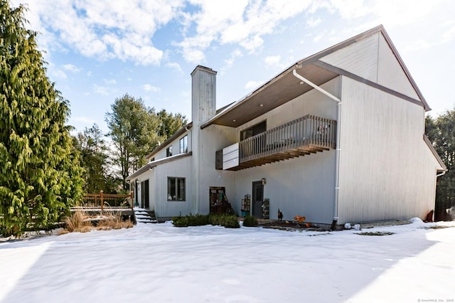 snow covered property with a chimney and a balcony