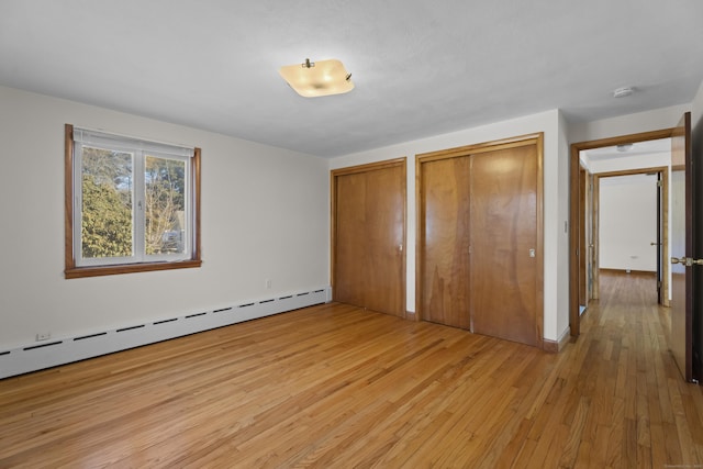 unfurnished bedroom with multiple closets, a baseboard radiator, and light wood finished floors