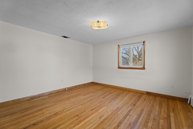 spare room with light wood finished floors, visible vents, and baseboards