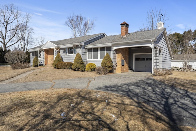 ranch-style home with a garage, driveway, a chimney, and roof with shingles