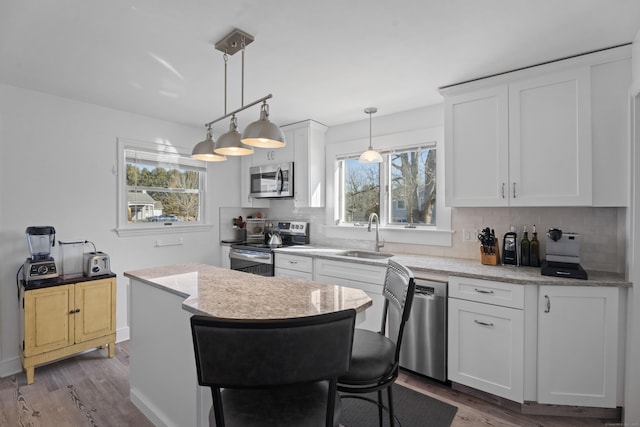 kitchen with tasteful backsplash, white cabinets, a kitchen island, stainless steel appliances, and a sink