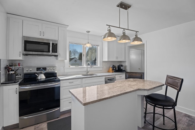 kitchen featuring a kitchen island, a sink, white cabinets, appliances with stainless steel finishes, and tasteful backsplash