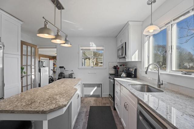 kitchen with white cabinets, radiator heating unit, stainless steel appliances, and a sink