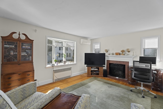 living area featuring a fireplace, wood finished floors, baseboards, a wall mounted AC, and radiator heating unit