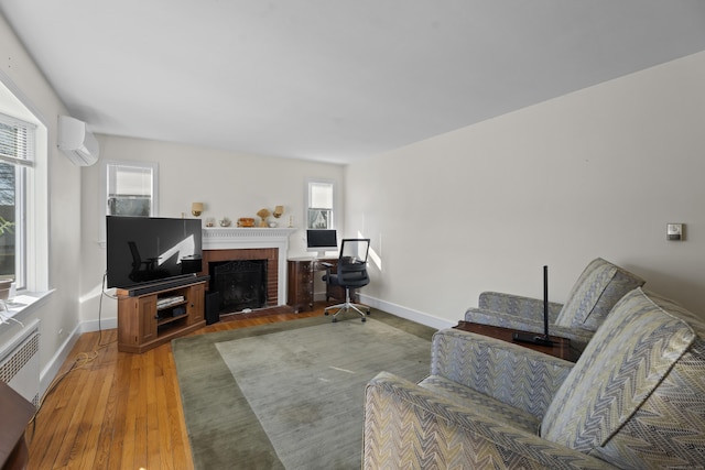 living room featuring a fireplace, a wall unit AC, wood finished floors, and baseboards