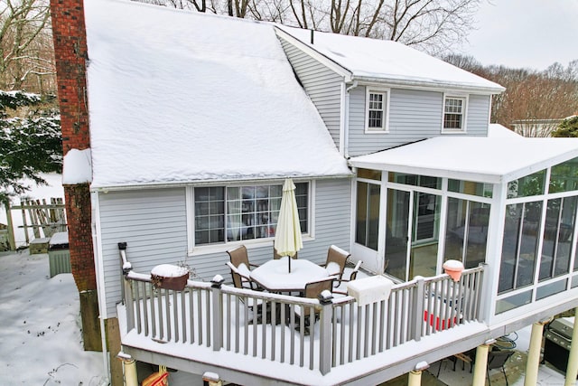 snow covered rear of property with a sunroom and a deck