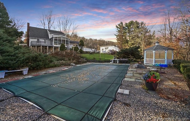 pool at dusk with a gazebo and a patio area