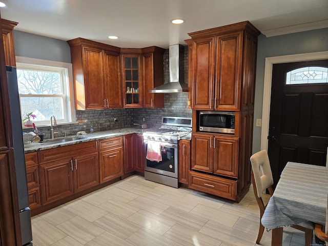 kitchen with wall chimney range hood, sink, stainless steel appliances, light stone countertops, and decorative backsplash