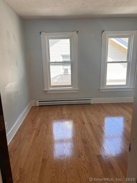 spare room featuring a baseboard radiator, plenty of natural light, light hardwood / wood-style flooring, and a textured ceiling