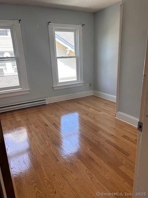 empty room featuring a baseboard radiator, light hardwood / wood-style floors, and a textured ceiling