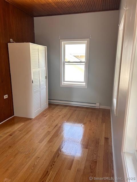 unfurnished bedroom with light wood-type flooring, wooden ceiling, and baseboard heating