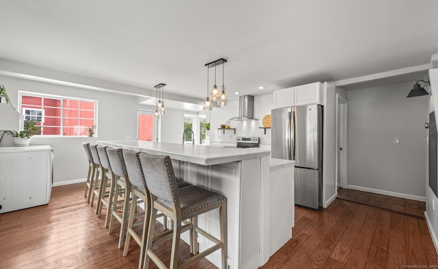 kitchen with white cabinets, appliances with stainless steel finishes, wall chimney range hood, a kitchen breakfast bar, and pendant lighting