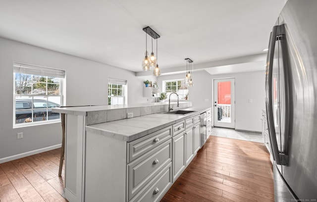 kitchen with light wood-type flooring, hanging light fixtures, stainless steel appliances, sink, and a kitchen bar