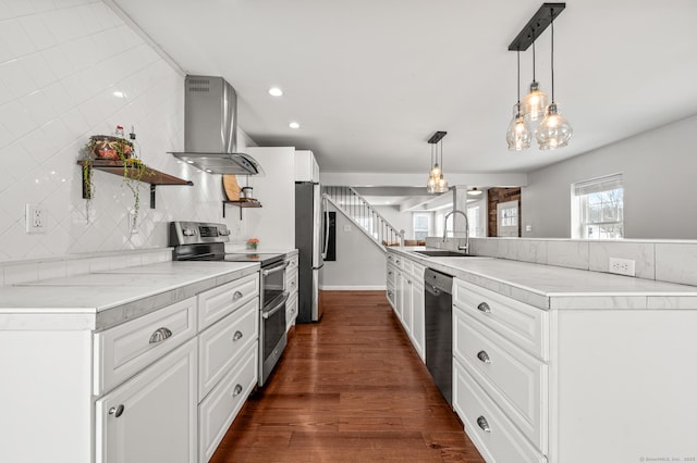 kitchen with appliances with stainless steel finishes, sink, white cabinetry, pendant lighting, and wall chimney exhaust hood