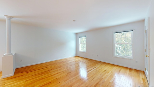 unfurnished room featuring decorative columns and light wood-type flooring