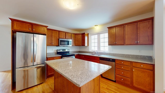 kitchen with a kitchen island, appliances with stainless steel finishes, sink, light hardwood / wood-style floors, and light stone countertops