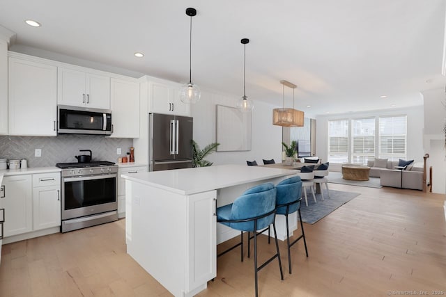 kitchen featuring white cabinetry, hanging light fixtures, appliances with stainless steel finishes, a kitchen breakfast bar, and a kitchen island