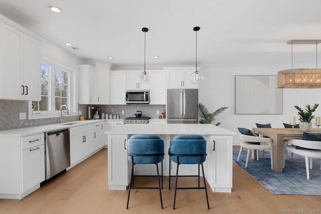 kitchen featuring sink, appliances with stainless steel finishes, hanging light fixtures, white cabinets, and a kitchen island