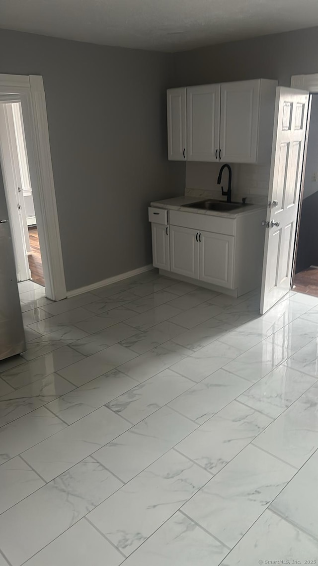 kitchen featuring white cabinetry, baseboards, marble finish floor, and a sink