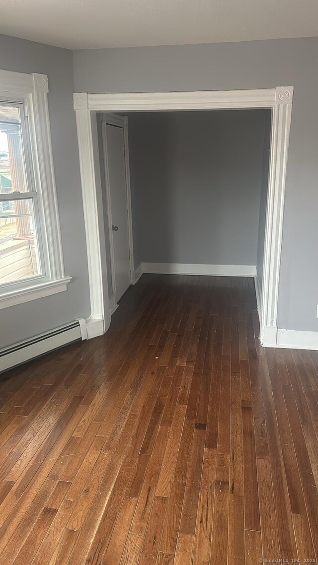 empty room featuring a baseboard heating unit, dark wood-type flooring, and baseboards