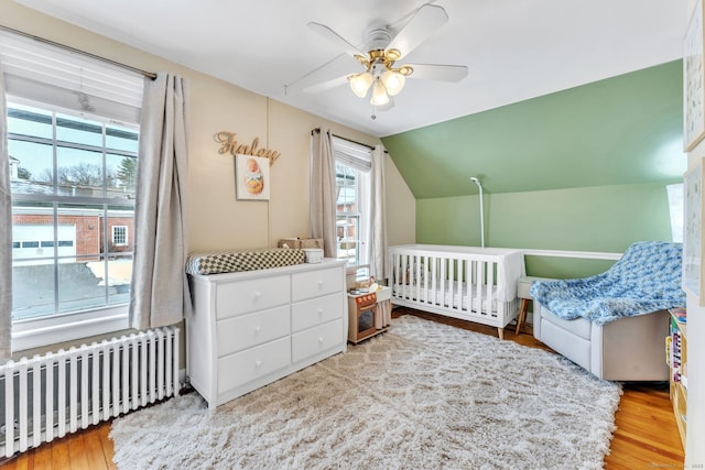 bedroom featuring radiator, lofted ceiling, ceiling fan, light hardwood / wood-style floors, and a crib