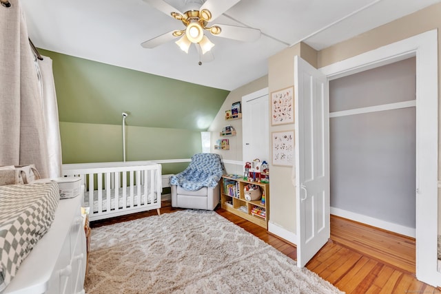 bedroom with hardwood / wood-style floors, vaulted ceiling, a crib, and ceiling fan