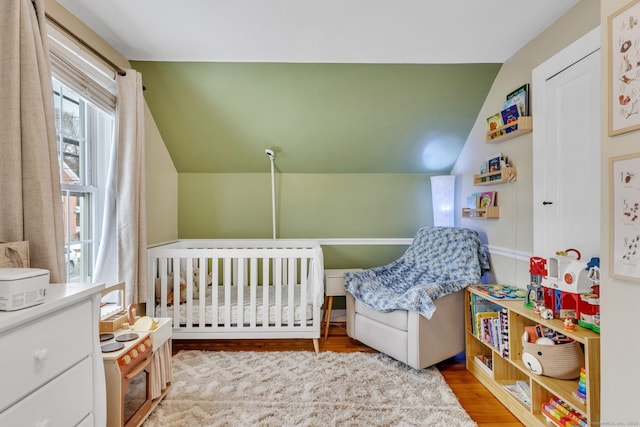 bedroom featuring vaulted ceiling, a nursery area, and light hardwood / wood-style floors