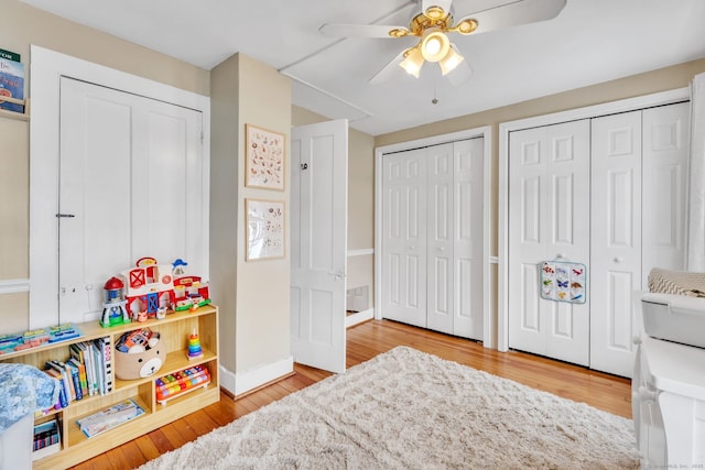 bedroom with two closets, light hardwood / wood-style floors, and ceiling fan