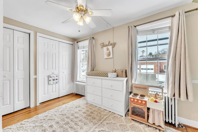 bedroom with radiator, two closets, hardwood / wood-style floors, and ceiling fan