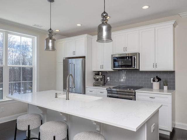 kitchen with white cabinetry, appliances with stainless steel finishes, a kitchen island with sink, and hanging light fixtures