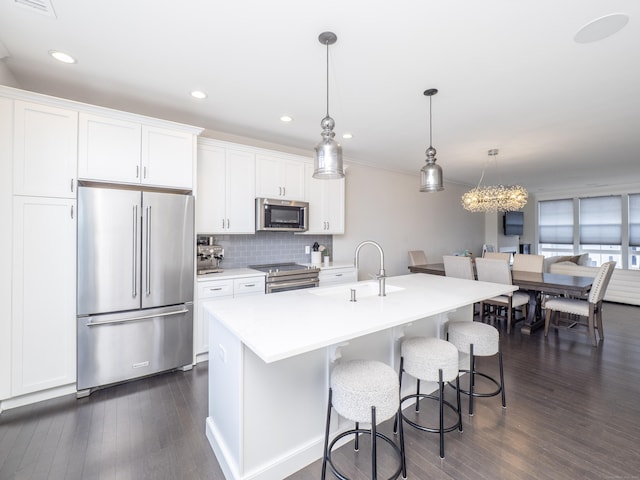 kitchen featuring sink, appliances with stainless steel finishes, pendant lighting, a kitchen island with sink, and white cabinets