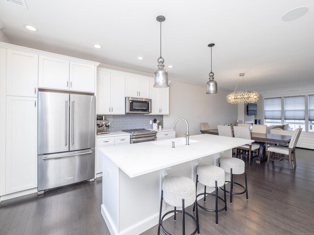 kitchen featuring a center island with sink, stainless steel appliances, white cabinetry, pendant lighting, and a sink