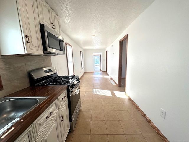 kitchen with light tile patterned floors, sink, stainless steel appliances, white cabinets, and a textured ceiling