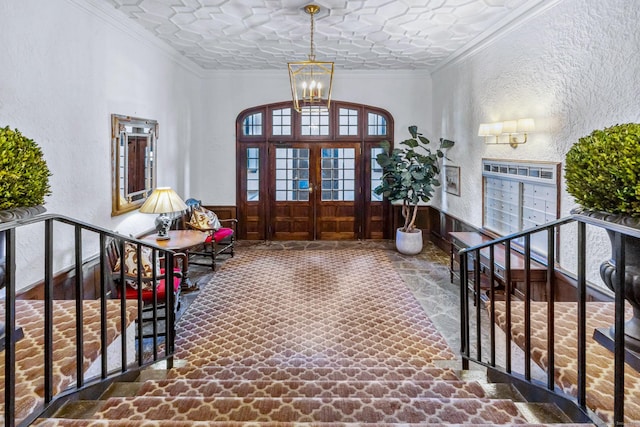 foyer entrance featuring a wainscoted wall, stone floors, ornamental molding, and a textured wall