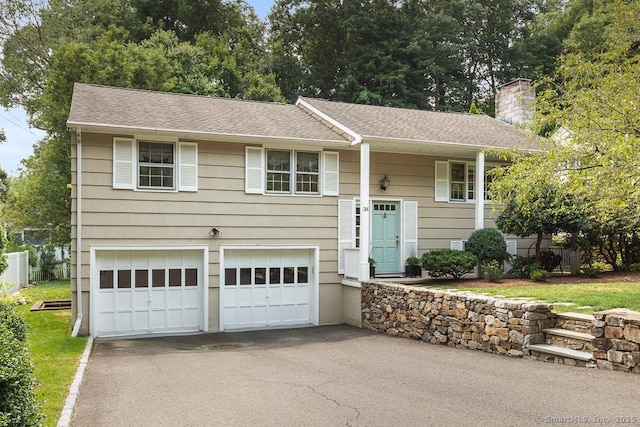 bi-level home with driveway, a garage, a chimney, and a shingled roof