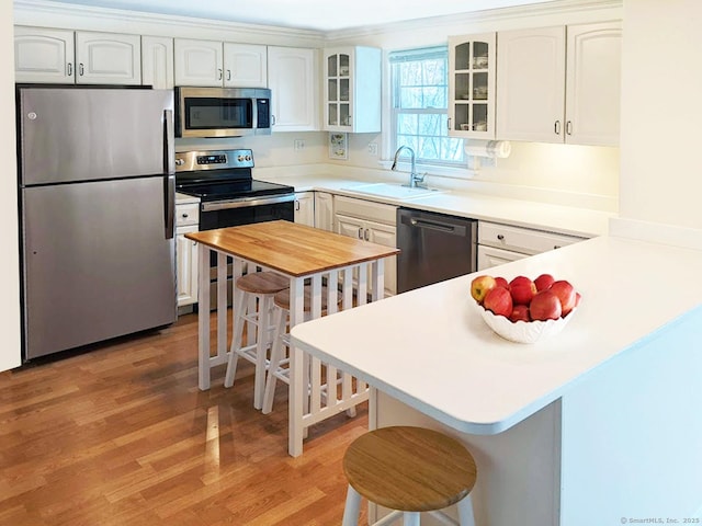 kitchen featuring a breakfast bar area, light countertops, appliances with stainless steel finishes, glass insert cabinets, and a sink