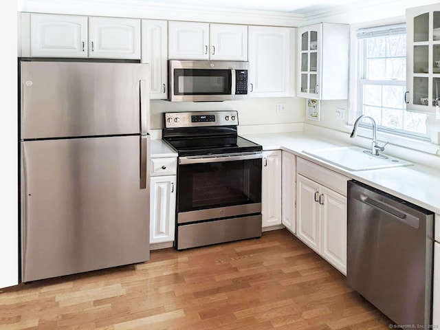 kitchen with appliances with stainless steel finishes, white cabinets, glass insert cabinets, and a sink