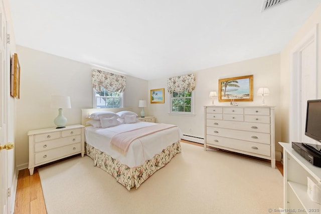 bedroom featuring light wood-type flooring, visible vents, and a baseboard heating unit