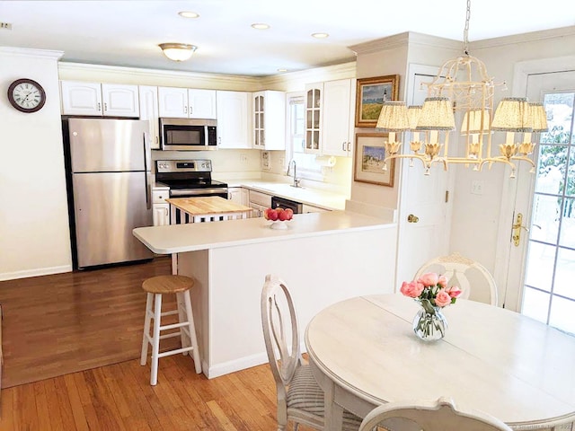 kitchen with glass insert cabinets, appliances with stainless steel finishes, hanging light fixtures, light countertops, and white cabinetry