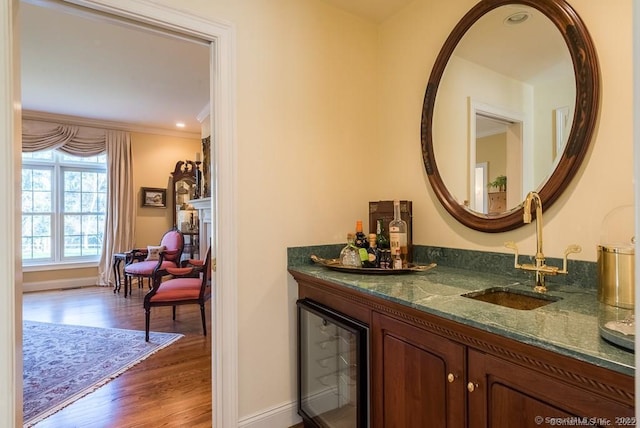 interior space with sink, wine cooler, wood-type flooring, ornamental molding, and dark stone counters