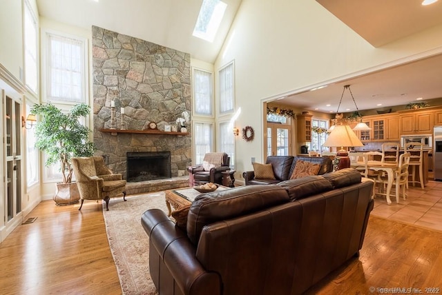 living room featuring high vaulted ceiling, a stone fireplace, a skylight, and light hardwood / wood-style floors