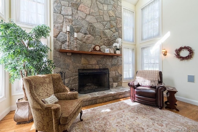 living area with a high ceiling, a stone fireplace, and light hardwood / wood-style floors