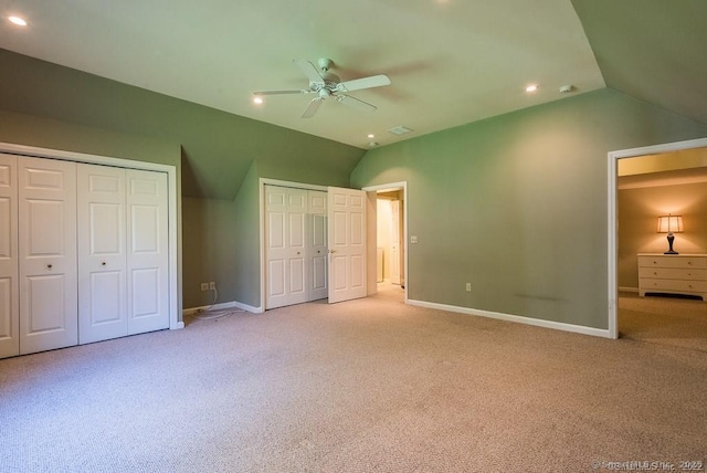 unfurnished bedroom featuring lofted ceiling, two closets, light carpet, and ceiling fan